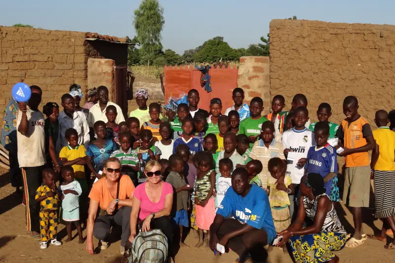 Gruppenfoto mit vielen Kindern und Helferinnen vor Lehmhäusern in Burkina Faso