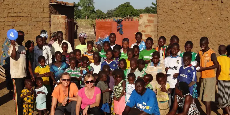 Gruppenfoto mit vielen Kindern und Helferinnen vor Lehmhäusern in Burkina Faso