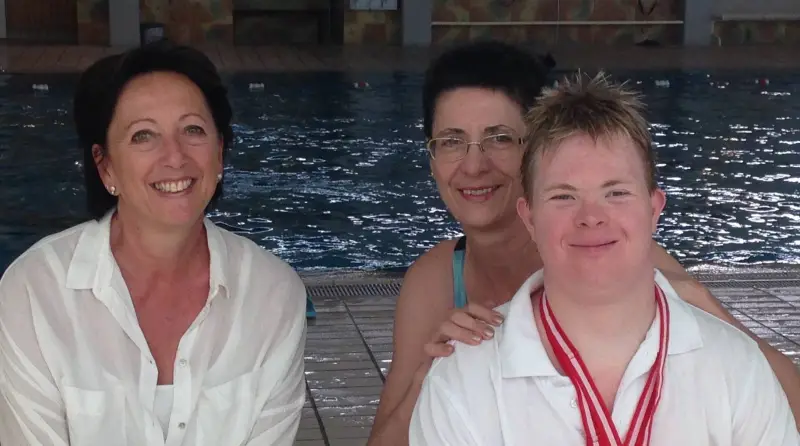 Schwimmer Sven mit Medaille und zwei Unterstützerinnen am Schwimmbecken