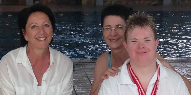 Schwimmer Sven mit Medaille und zwei Unterstützerinnen am Schwimmbecken