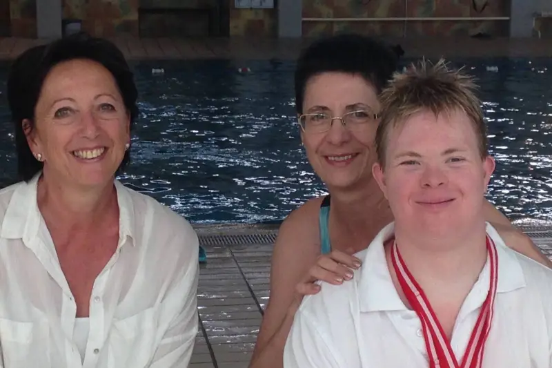 Schwimmer Sven mit Medaille und zwei Unterstützerinnen am Schwimmbecken