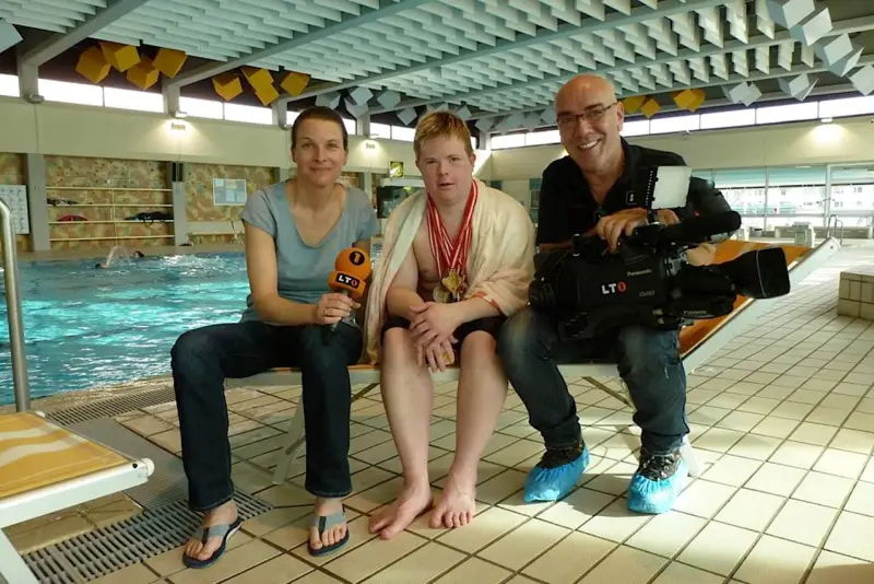 Schwimmer Sven mit Medaillen bei einem Fernsehinterview am Schwimmbecken