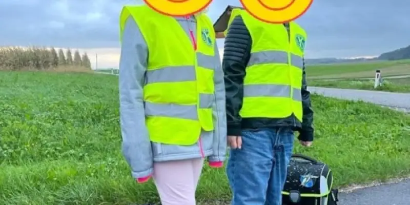 Zwei Kinder mit Warnwesten und Schultaschen am Straßenrand