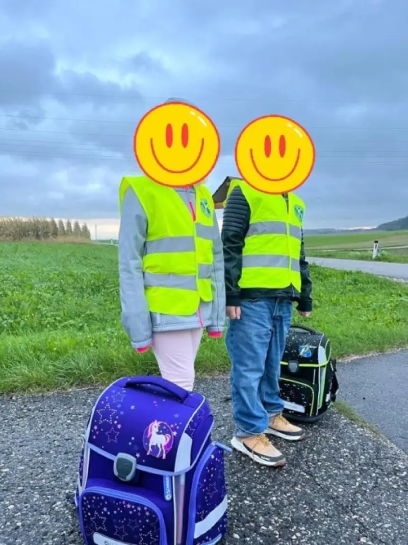 Zwei Kinder mit Warnwesten und Schultaschen am Straßenrand