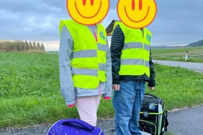 Zwei Kinder mit Warnwesten und Schultaschen am Straßenrand